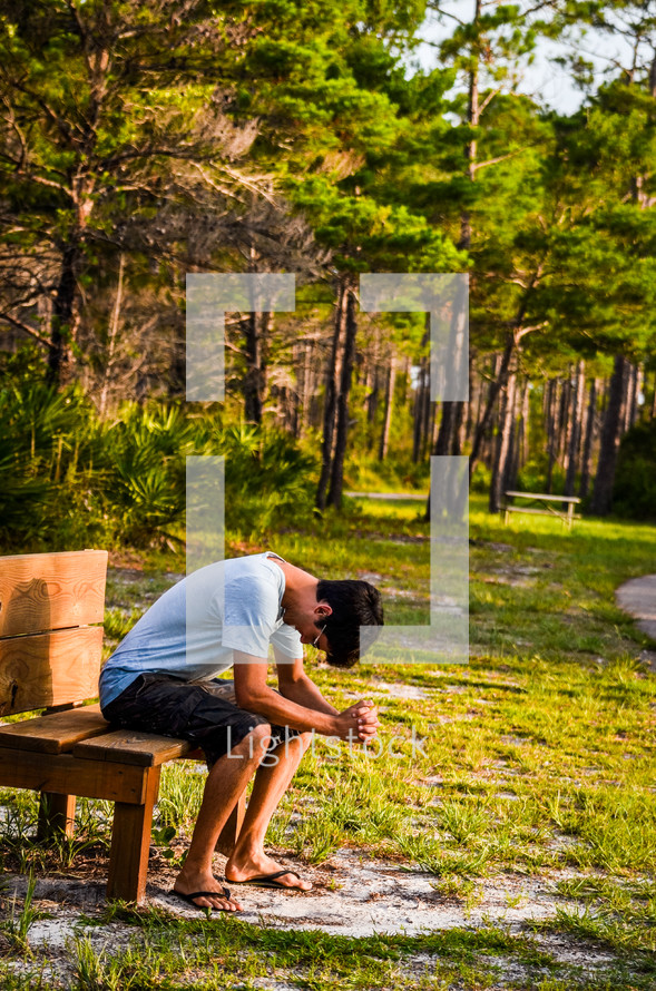 man sitting in prayer on a bench outdoors