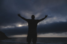 a man standing in a storm with arms raised praying to God 