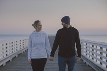 a couple standing on a pier holding hands 