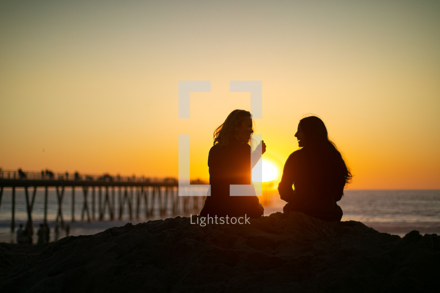 two women sitting on a beach talking 