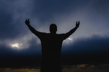 a man standing in a storm with arms raised praying to God 