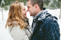 a couple nose to nose standing outdoors in snow 
