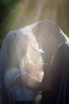 bride and groom kissing under a veil 
