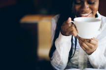 woman holding a coffee mug to her mouth over a Bible