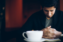 man with his head bowed in prayer at a coffee house