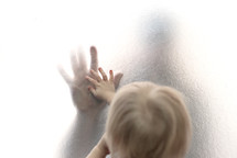 child touching parent's hand through frosted glass 