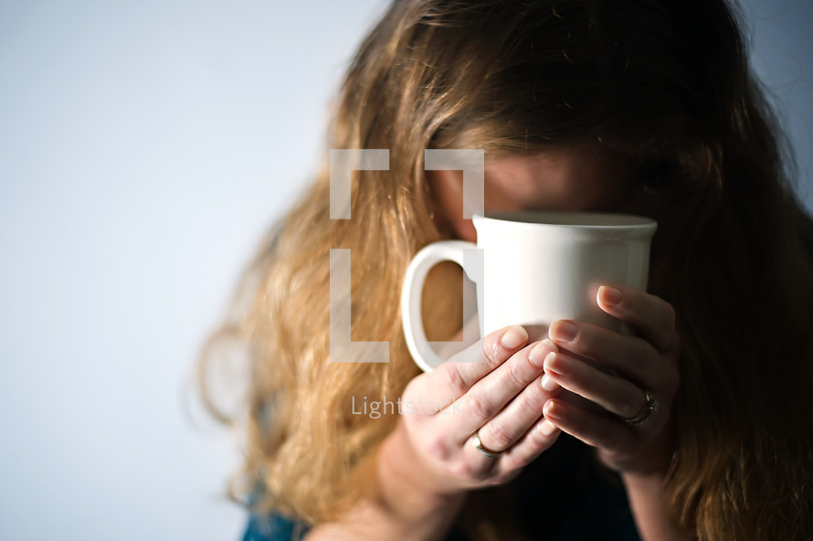 woman holding a mug of coffee with head bowed in prayer