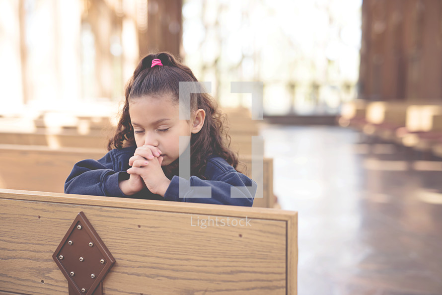 a little girl praying in church pews 