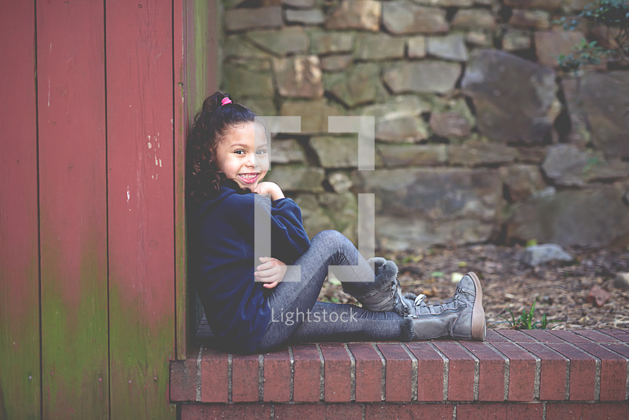 portrait of a girl child sitting on a brick ledge 