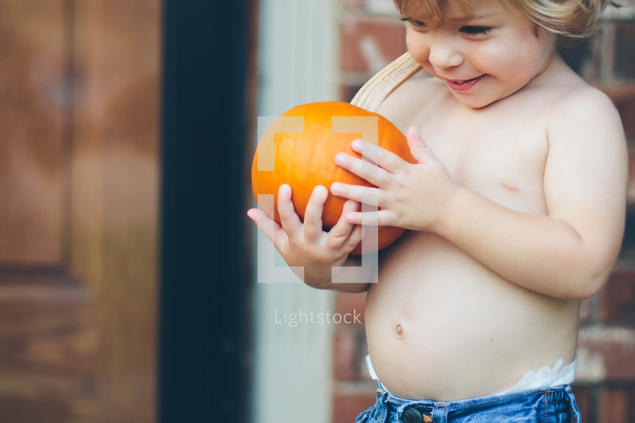 a toddler boy holding a pumpkin 
