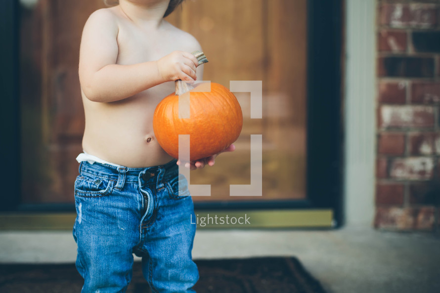 toddler holding a pumpkin on a  porch 