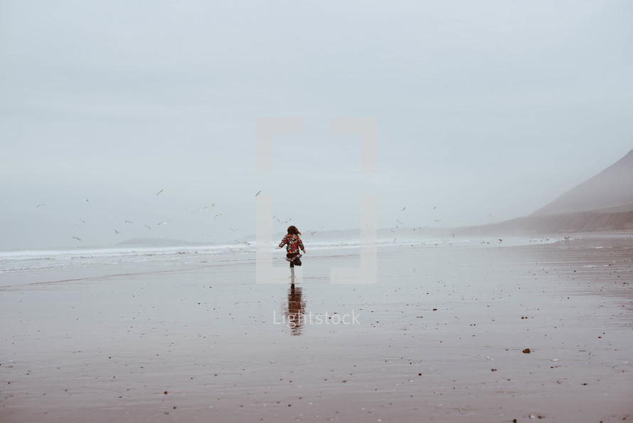 a little girl running on a beach in a coat in winter 