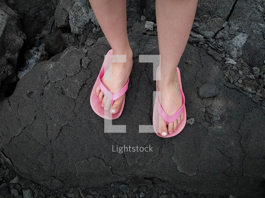 feet in flip flops standing on volcanic rock