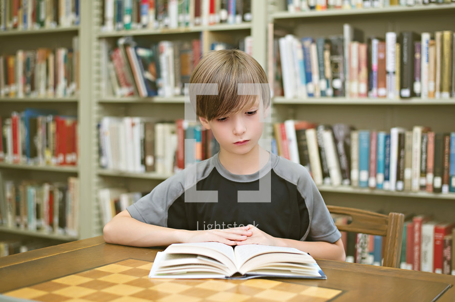 Boy reading a book on a table in a library.