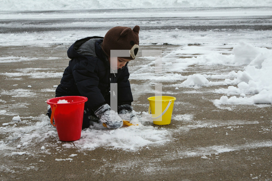 a child playing with snow in a driveway 
