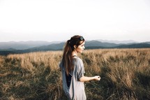a woman walking through a field of tall grass on a mountain top 