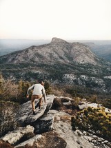 man climbing up a rock on the edge of a mountainside 