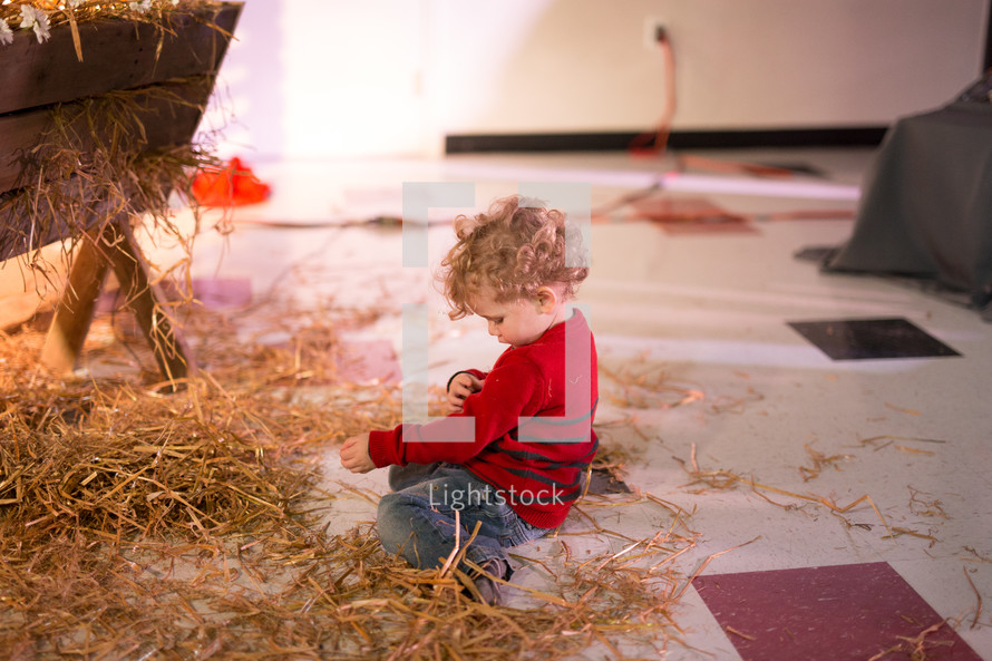 a child playing in straw by a manger 