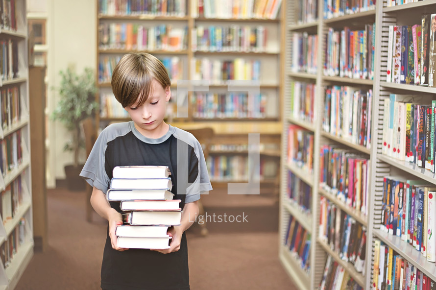 Boy carrying a stack of books in a library.