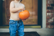 toddler holding a pumpkin on a  porch 