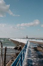 Ice covered railing on beach pier leading out to a lighthouse on Lake Michigan
