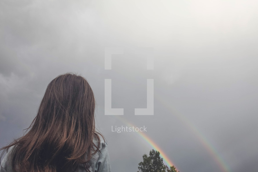girl looking up at a rainbow in the sky 
