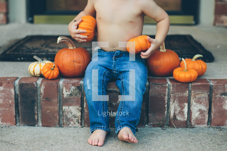 toddler boy sitting on steps with pumpkins 