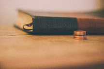 Bible and a stack of pennies on a wooden table.