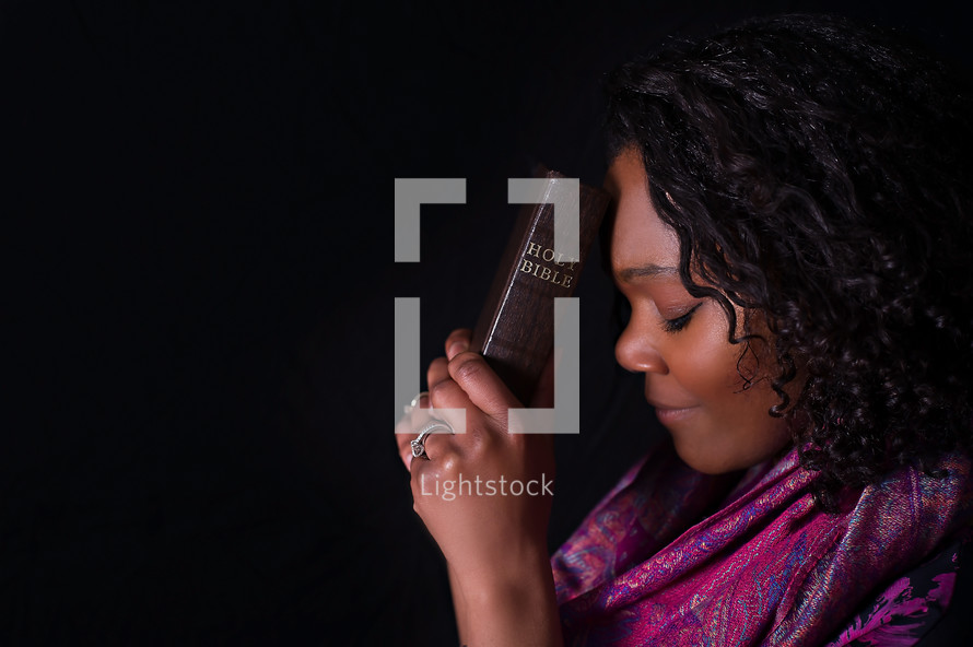 African American woman holding a Bible to her head 