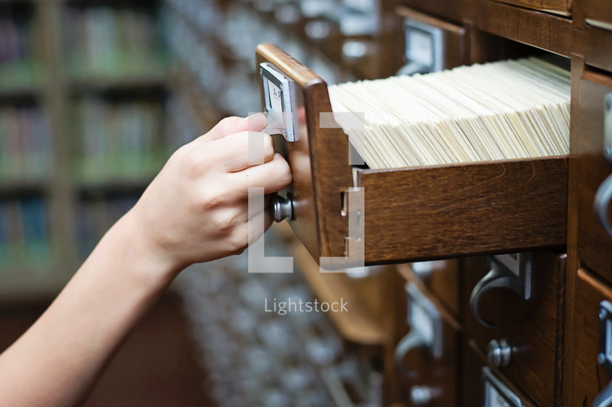Library card catalog cabinet with a hand opening drawer.