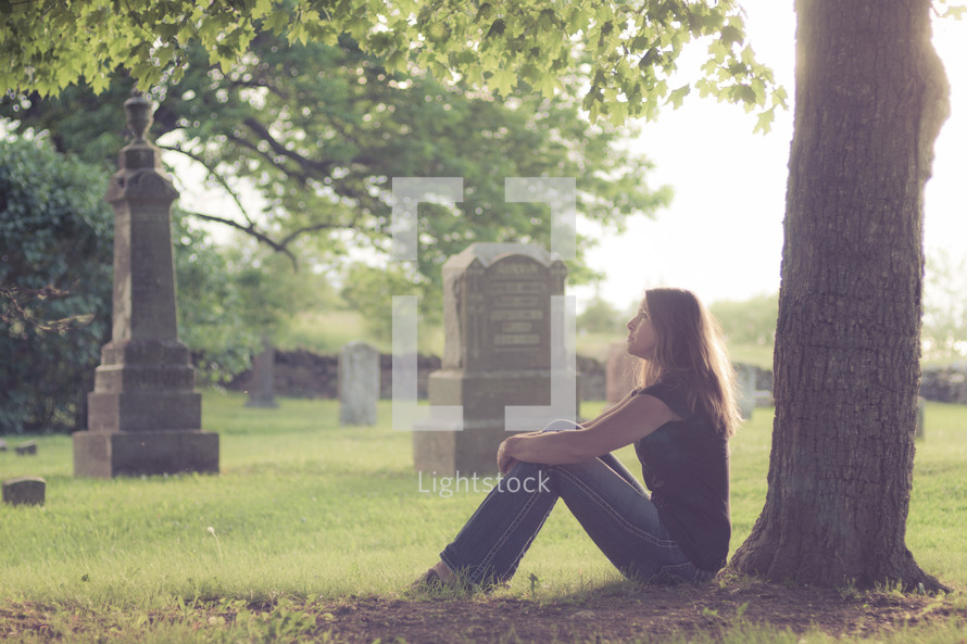 woman sitting in front of a tree in a cemetery 