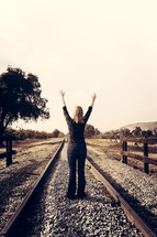 woman with arms raised on railroad tracks 