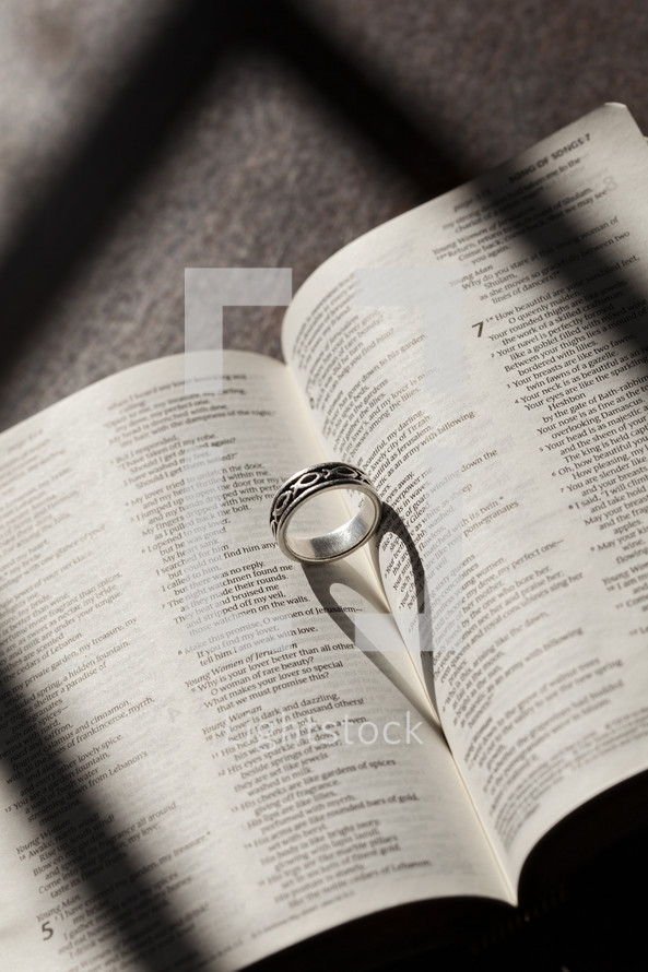 Wedding band in the pages of a Bible forming a heart shadow 