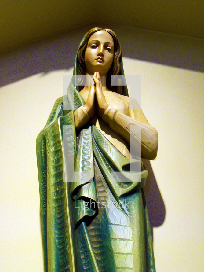 A colorful statue of Mary, the mother of Jesus, wearing emerald green robes and hands clasped together in prayer and worship to God.  
