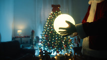 Santa claus putting a light ball under the Christmas tree