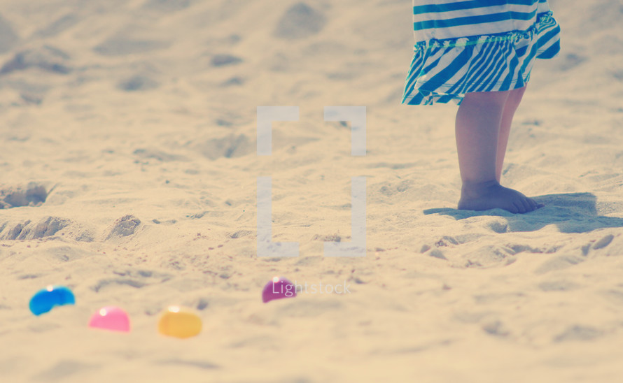 Child's legs on the beach with Easter eggs.