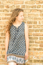 woman in a dress leaning against a brick wall 