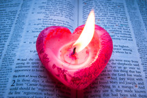 A pink heart-shaped candle burns on a bible opened at Luke chapter 2.