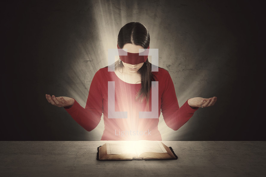 A woman reading a glowing Bible wearing a blindfold. 