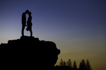 silhouette of an expecting couple standing at the edge of a cliff at dusk 