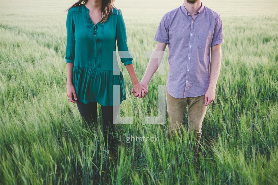 A man and woman hold hands in a field of green grass.