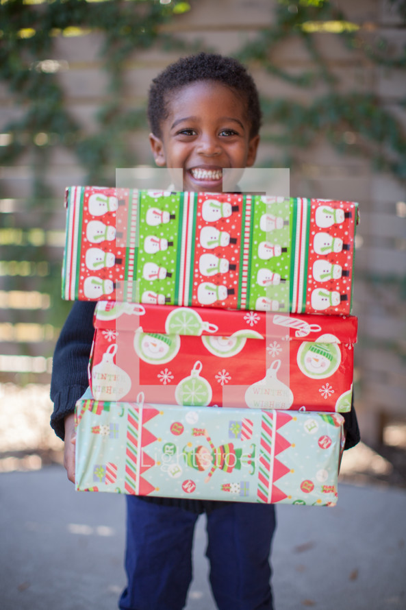 boy child holding stacked Christmas gifts 