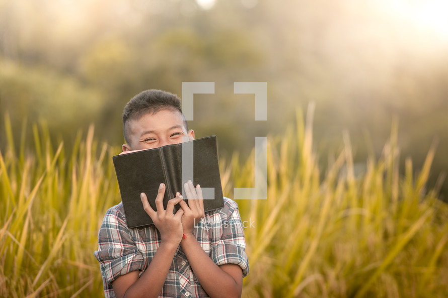 a boy reading a Bible in a rice field