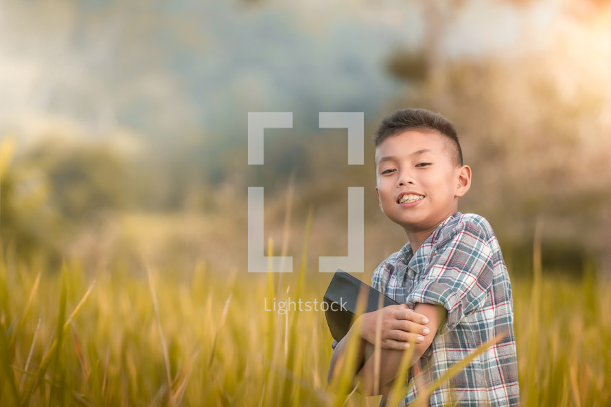 a boy holding a Bible standing in a rice field 