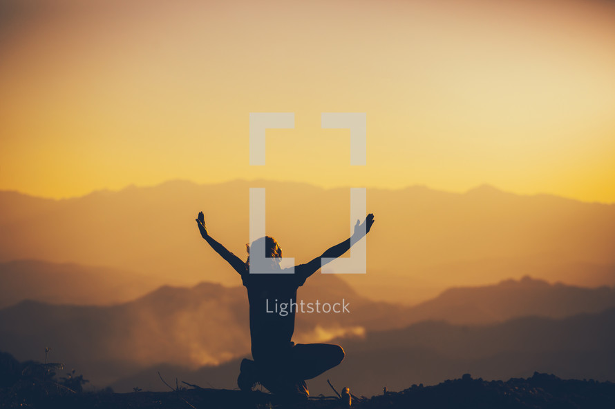 silhouette of a person with raised hands at sunset on a mountaintop 