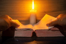 candle light with hands reading bible on wooden table in the night time.