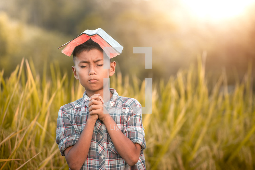 a boy holding a Bible standing in a rice field 