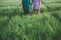 A man and woman holding hands in a field of green grass.