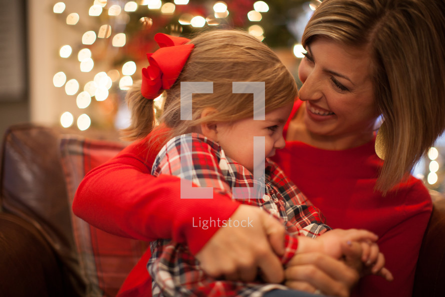 mother and daughter snuggling in front of a Christmas tree 