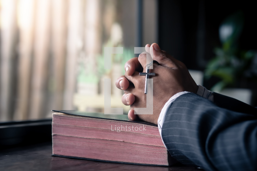 Close up hands of christian man praying with a cross on Bible